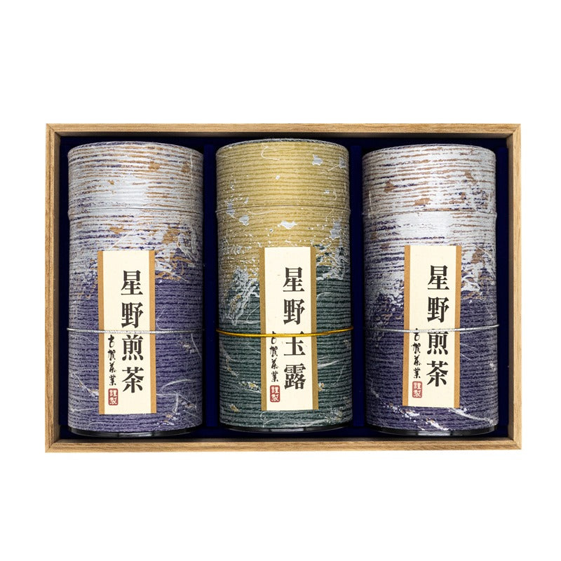 Front view of three purple and golden tube-shaped green tea boxes placed inside a wooden box with Japanese markings on them mentioning their origins (Hoshino sencha and gyokuro).