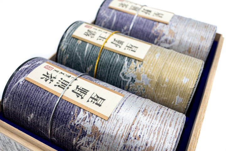 Close view of three purple and golden tube-shaped green tea boxes with Japanese markings on them mentioning their origins (Hoshino sencha and gyokuro).