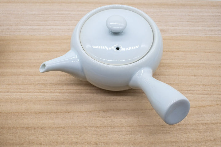 Japanese tea pot in white porcelain made in Arita, Japan, made for brewing gyokuro green tea, with a side handle, placed on a wooden plank.