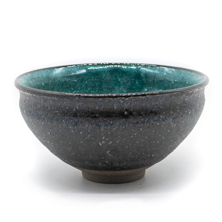 Front side of a matcha bowl, with a dark grey and rough outside and a vibrant and glazed turquoise color on the inside.