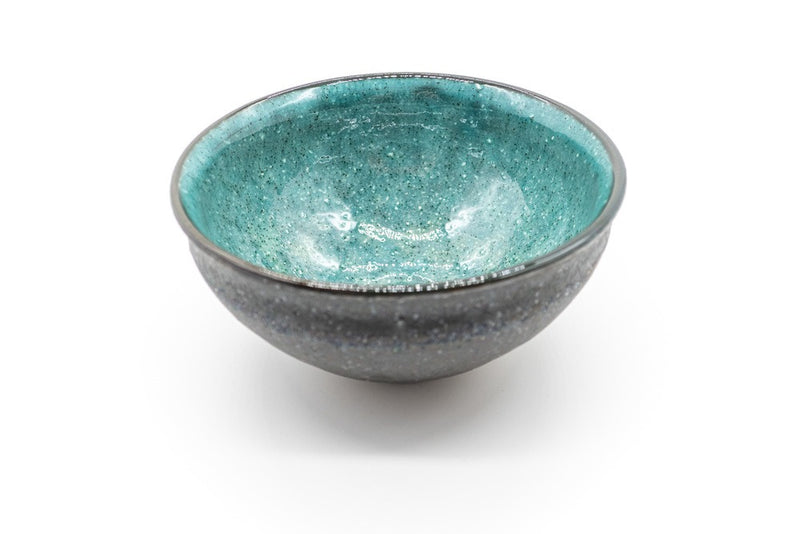 Inside of a matcha bowl, with a dark grey and rough outside and a vibrant and glazed turquoise color on the inside.