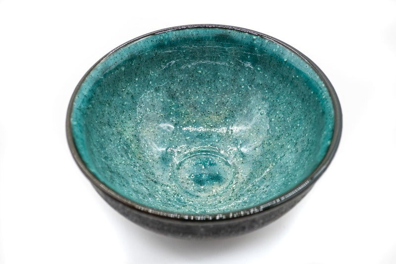 Inside of a matcha bowl, with a dark grey and rough outside and a vibrant and glazed turquoise color on the inside.