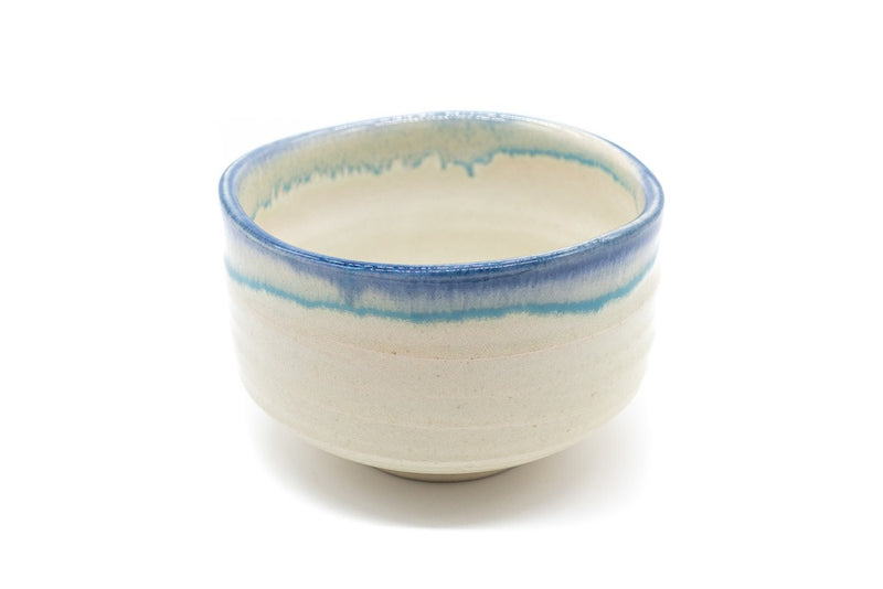 Front of a cream-white matcha bowl with a blue-colored glaze all around its uneven edge.