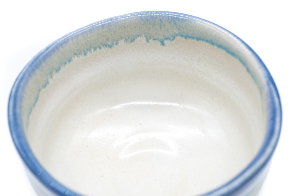 Intérieur d'un bol à matcha couleur blanc crème avec une glaçure de couleur bleue tout autour de son bord irrégulier. L'intérieur est recouvert d'une glaçure blanche.