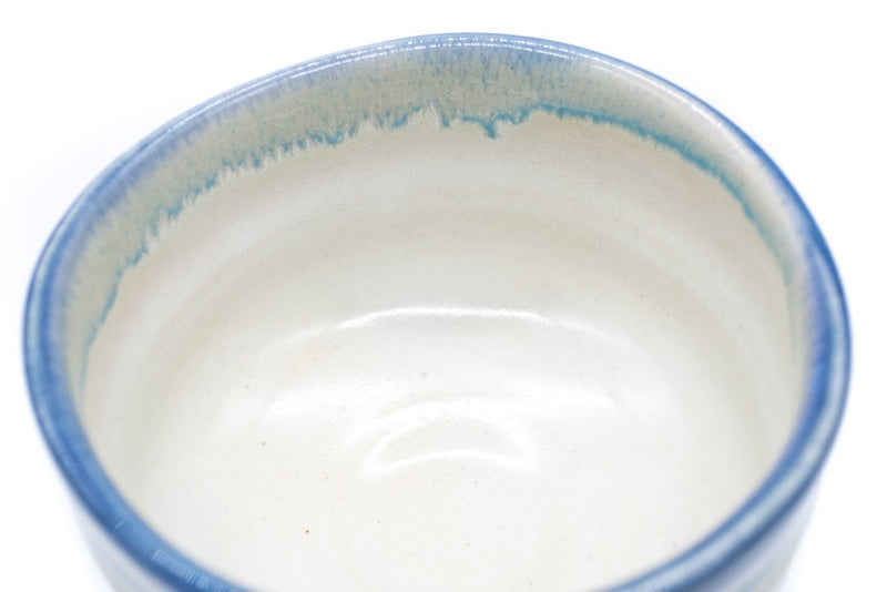Inside of a cream-white matcha bowl with a blue-colored glaze all around its uneven edge. The inside is covered with white glaze.