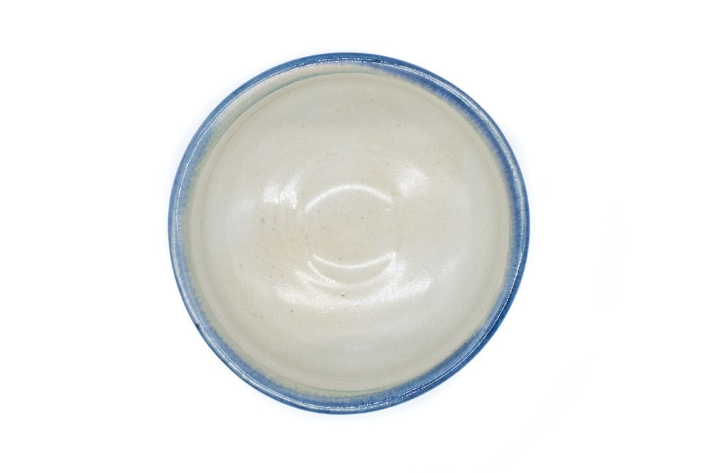 Intérieur d'un bol à matcha couleur blanc crème avec une glaçure de couleur bleue tout autour de son bord irrégulier. L'intérieur est recouvert d'une glaçure blanche.