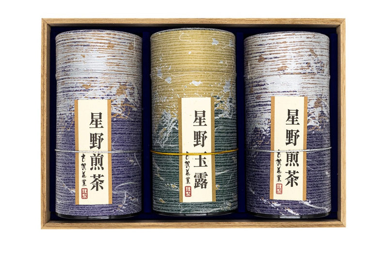 Front view of three purple and golden tube-shaped green tea boxes placed inside a wooden box with Japanese markings on them mentioning their origins (Hoshino sencha and gyokuro).