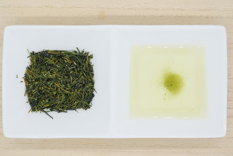 Top view of a rectangular porcelain dish, with one square filled with needle-shaped leaves of Japanese premium white tea from Yame, and the other with pale-white brewed white tea.