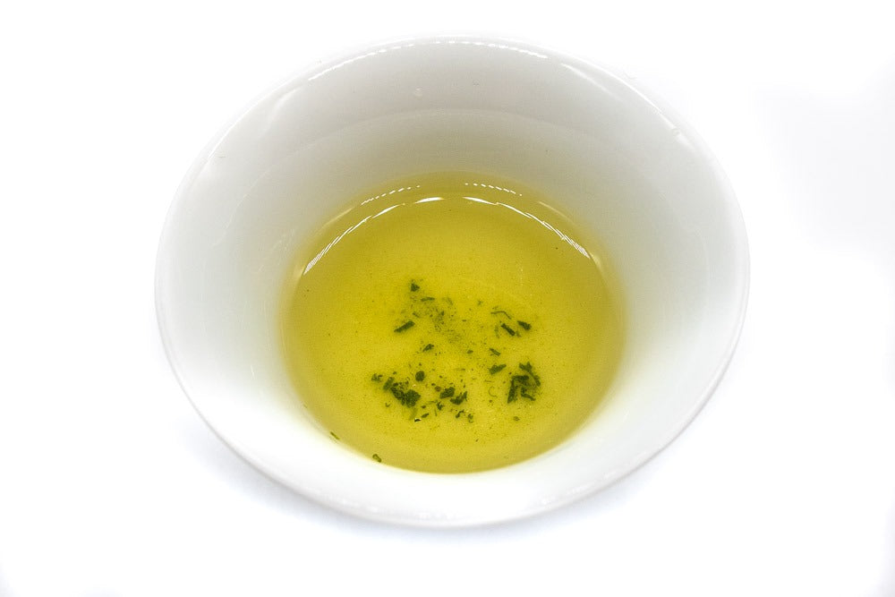 Top view of a small white porcelain cup against a white background filled with golden-green brewed dento hon gyokuro green tea from Yame.