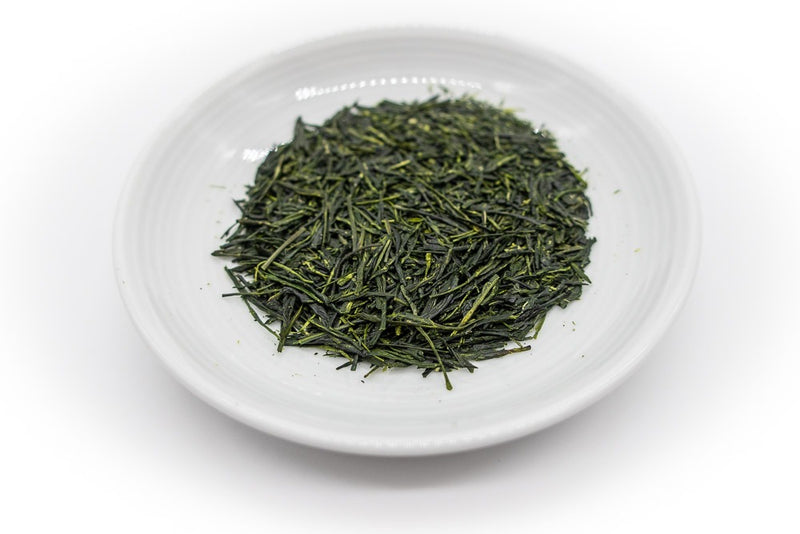 Needle-shaped and deep emerald green dento hon gyokuro leaves from Yame, Japan, in a circle shape, on a small round white dish..