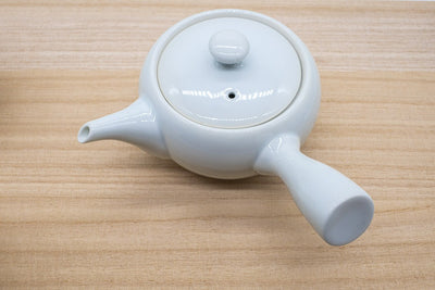 Japanese tea pot in white porcelain made in Arita, Japan, made for brewing gyokuro green tea, with a side handle, placed on a wooden plank.