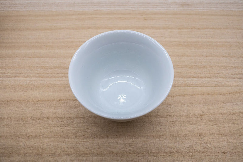 Small Japanese tea cup in white porcelain made in Arita, Japan, made for drinking gyokuro green tea, placed on a wooden plank.