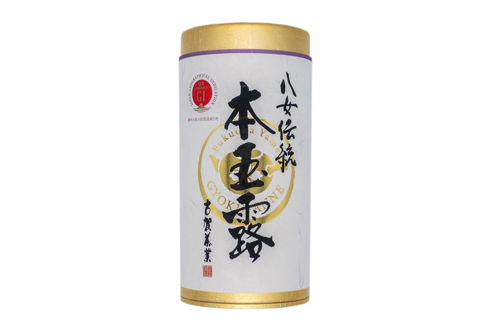 Tube-shaped golden box with a white paper label wrapped around it with hand-written Japanese calligraphy on it, with the words 'dento hon gyokuro, Yame tea'.