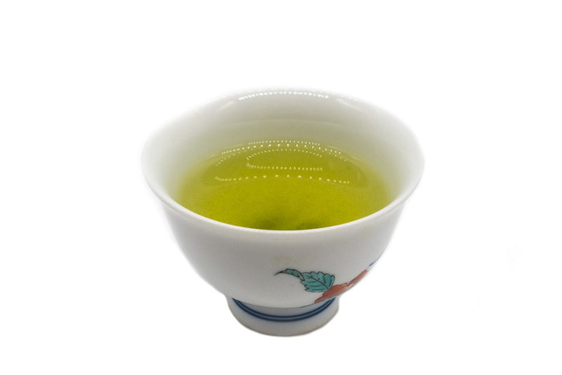 Side view of a small white porcelain cup filled with brewed premium Japanese sencha green tea.